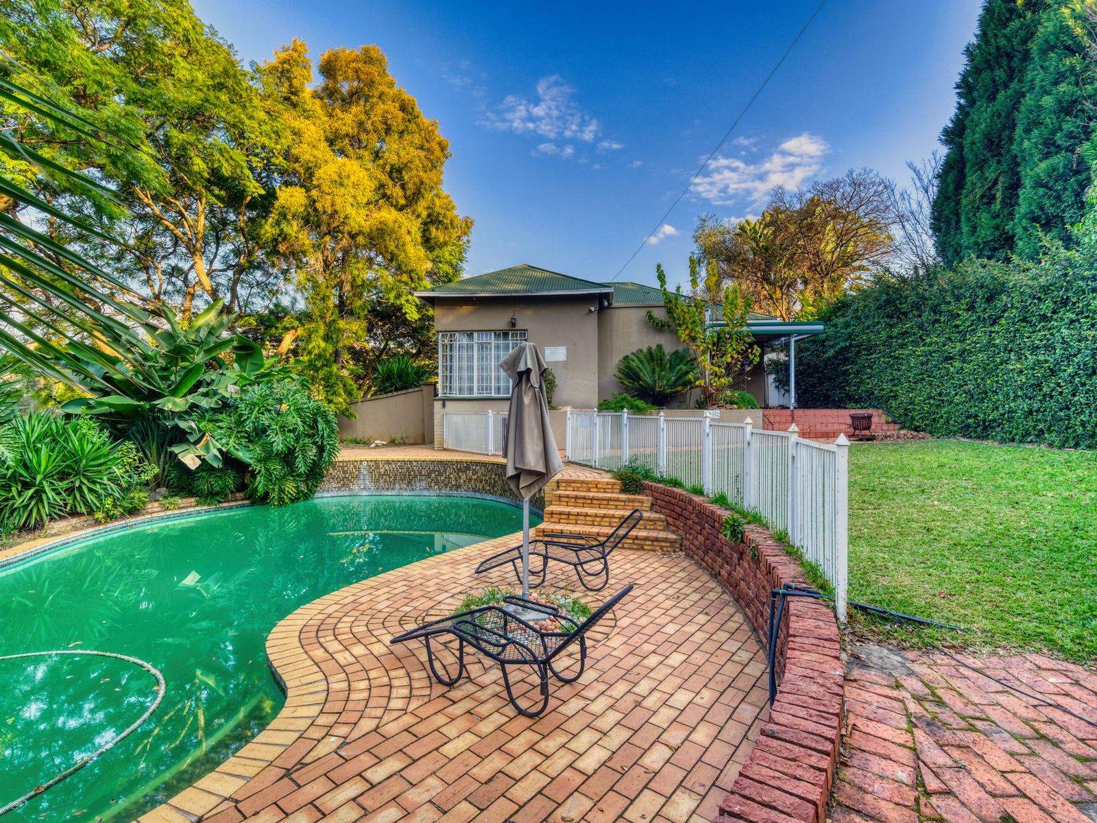 Curved brick paver pool deck with steps and a retaining wall in a backyard